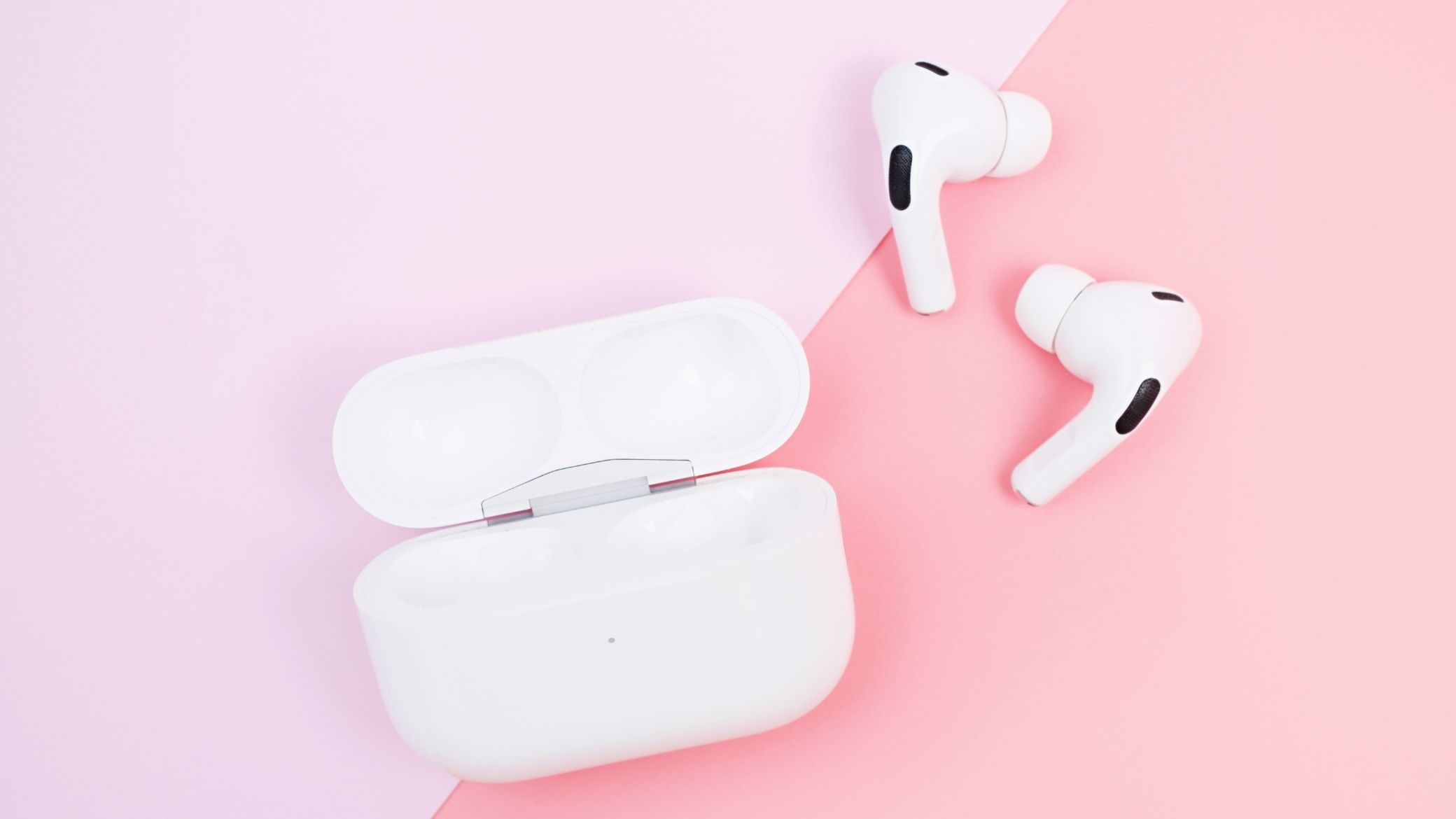 Boîtier d'écouteurs intra-auriculaires blancs avec embouts en silicone sur fond rose pastel bicolore, plan flat-lay éditorial illustrant le format intra-auriculaire moderne compatible avec la réduction de bruit active
