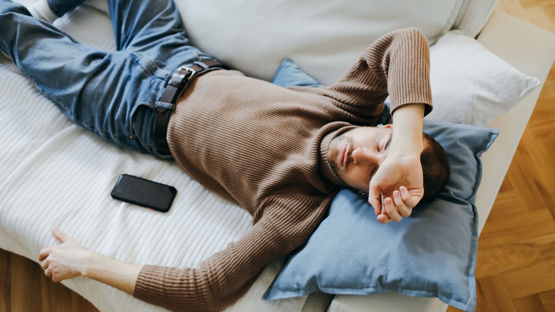 Hombre dormido completamente vestido sobre una cama, smartphone colocado a su lado, ilustrando el hecho de dormirse con una fuente de audio activa por la noche